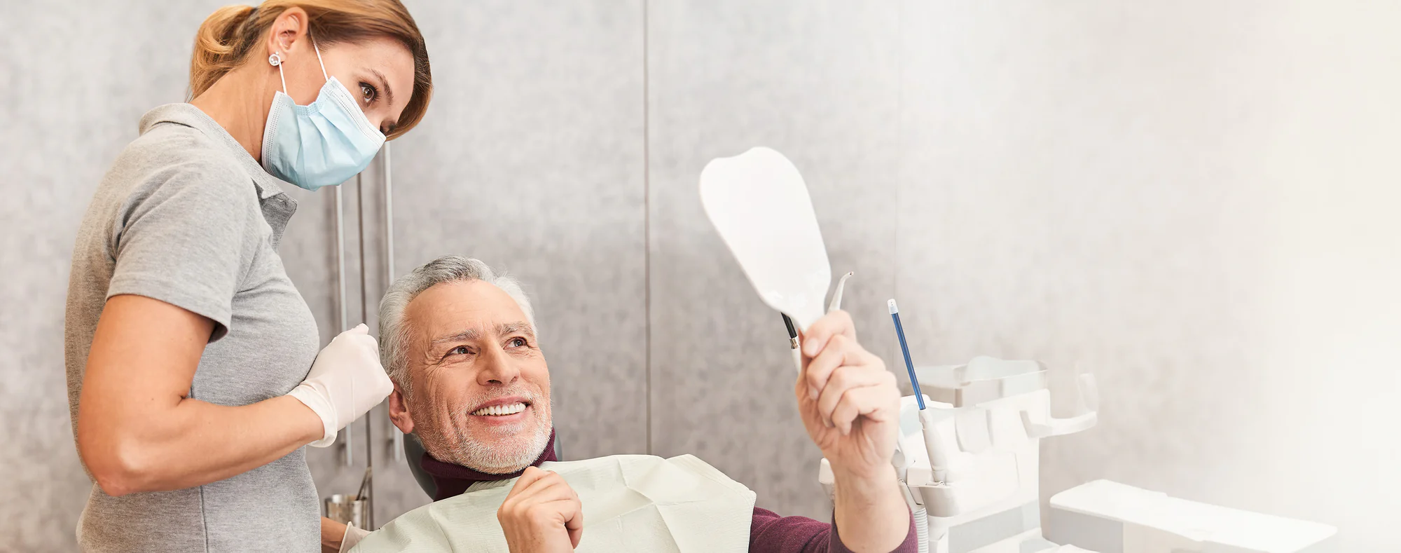 Ein Mann lächelt und betrachtet seine Zähne im Spiegel während einer Zahnbehandlung bei einem Zahnarzt.